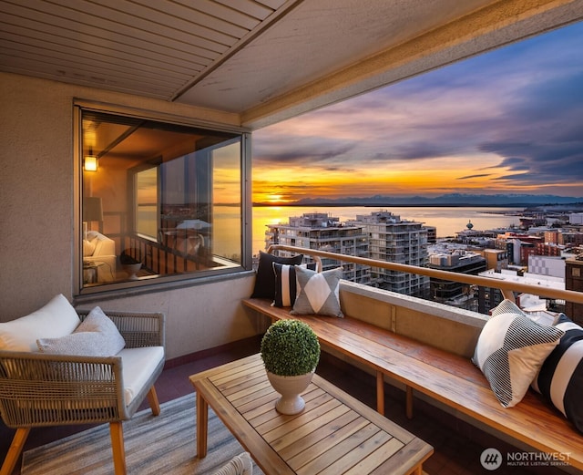 balcony at dusk with a water view and a view of city