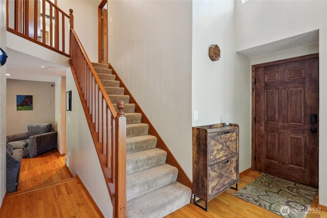 entryway featuring stairs, baseboards, wood finished floors, and a towering ceiling