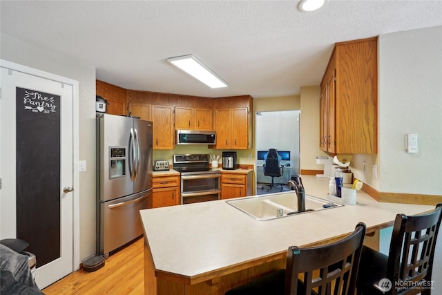 kitchen with appliances with stainless steel finishes, brown cabinets, a sink, light countertops, and a peninsula