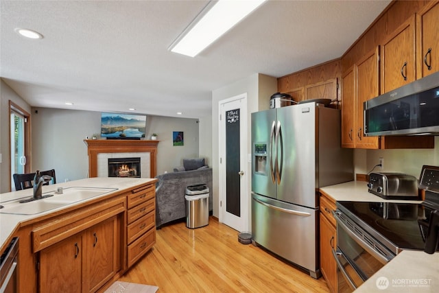 kitchen featuring a sink, appliances with stainless steel finishes, brown cabinetry, and light countertops