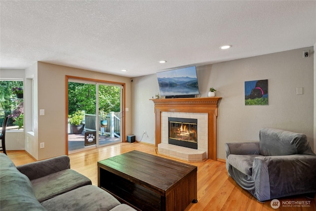 living area with a tiled fireplace, recessed lighting, light wood-type flooring, and a textured ceiling