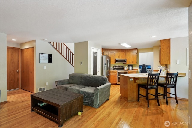 living area featuring a textured ceiling, stairs, recessed lighting, light wood-type flooring, and visible vents