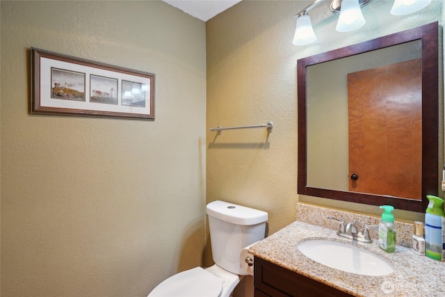bathroom featuring vanity, a textured wall, and toilet