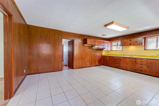 kitchen featuring brown cabinetry, light countertops, a sink, wooden walls, and under cabinet range hood