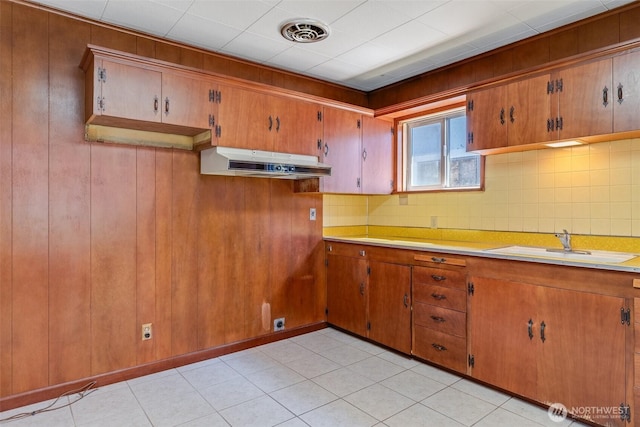 kitchen featuring a sink, light countertops, under cabinet range hood, and brown cabinets