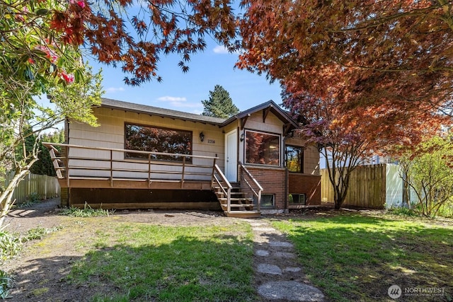 view of front of house with fence, a wooden deck, a front lawn, and brick siding