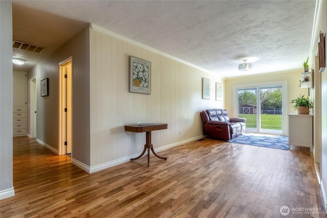 living area featuring wood finished floors, visible vents, ornamental molding, and baseboards