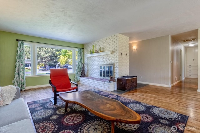 living room with a brick fireplace, visible vents, baseboards, a textured ceiling, and wood finished floors