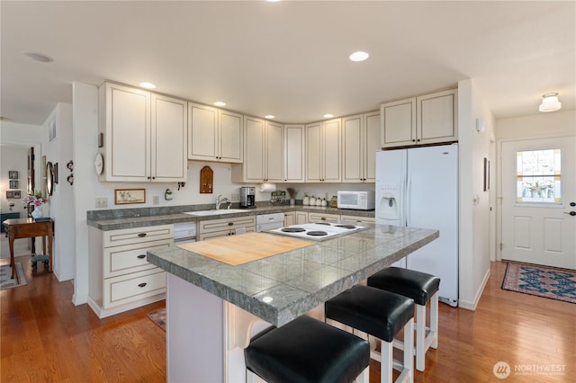 kitchen featuring a breakfast bar, wood finished floors, white appliances, and a sink