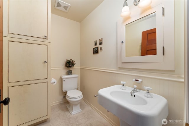 half bathroom with a sink, visible vents, a wainscoted wall, toilet, and a decorative wall