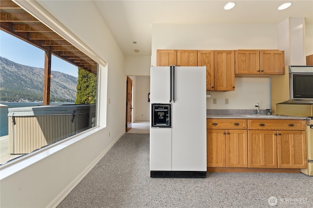 kitchen featuring recessed lighting, white refrigerator with ice dispenser, stainless steel microwave, brown cabinetry, and a mountain view