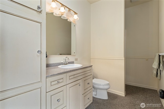 bathroom with vanity, toilet, a wainscoted wall, and baseboards
