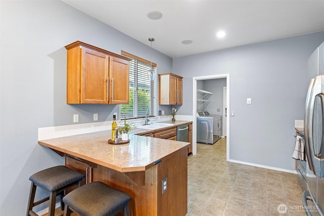 kitchen with brown cabinets, stainless steel appliances, a sink, washer and dryer, and a peninsula