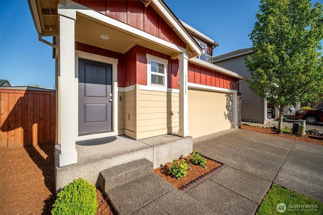 view of exterior entry featuring concrete driveway, an attached garage, fence, and board and batten siding