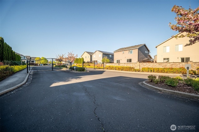 view of road featuring a gate, a residential view, curbs, and a gated entry
