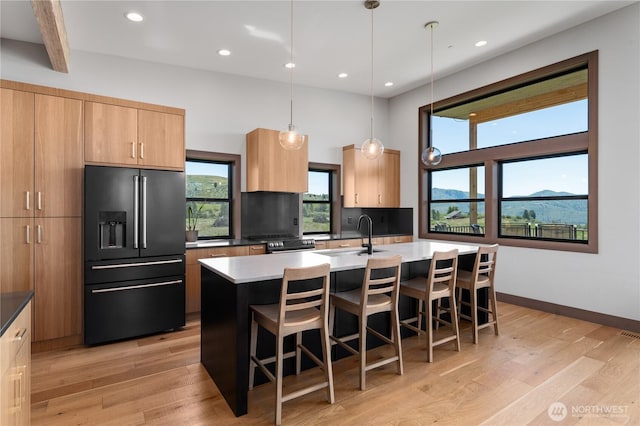 kitchen with high end black refrigerator, a sink, stove, a kitchen island with sink, and a breakfast bar area