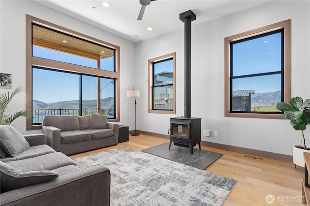 living area featuring a wood stove, a mountain view, a ceiling fan, light wood-type flooring, and recessed lighting