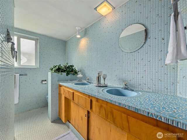 bathroom with double vanity, a sink, tile patterned flooring, and tile walls