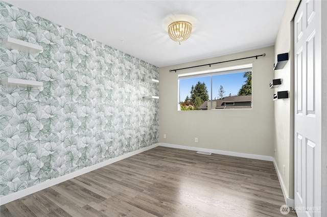 2524 171st St SE, Bothell, WA 98012 - empty room featuring wallpapered walls, baseboards, an accent wall, wood finished floors, and a chandelier