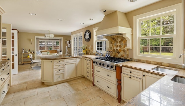kitchen featuring a peninsula, cream cabinetry, custom range hood, a sink, and stainless steel gas stovetop