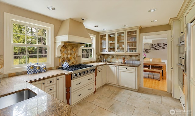 kitchen with backsplash, stainless steel appliances, cream cabinetry, and custom range hood