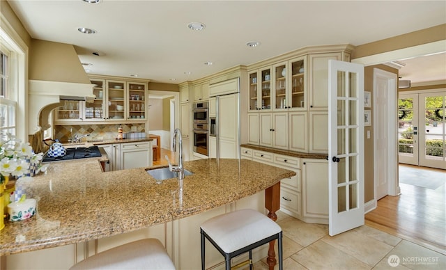 kitchen featuring cream cabinets, tasteful backsplash, a sink, light stone counters, and a peninsula