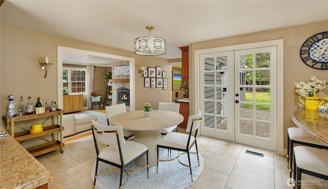 dining room featuring french doors, a lit fireplace, visible vents, and a wealth of natural light