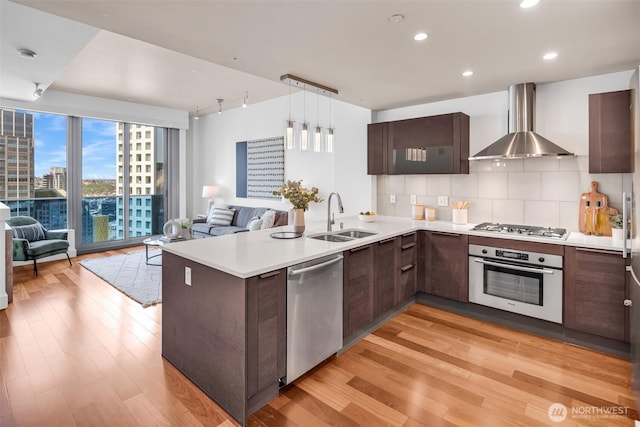 737 Olive Way Unit 3101, Seattle, WA 98101 - kitchen featuring stainless steel appliances, wall chimney range hood, a sink, open floor plan, and a peninsula