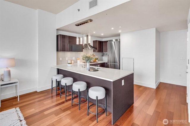 737 Olive Way Unit 3101, Seattle, WA 98101 - kitchen featuring stainless steel fridge, dark brown cabinets, wall chimney range hood, light countertops, and a kitchen bar
