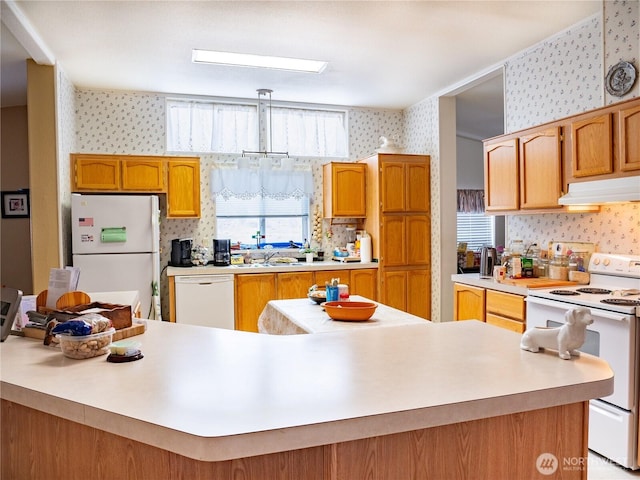 kitchen featuring brown cabinets, wallpapered walls, under cabinet range hood, light countertops, and white appliances