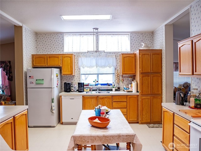 kitchen with wallpapered walls, light floors, light countertops, a sink, and white appliances