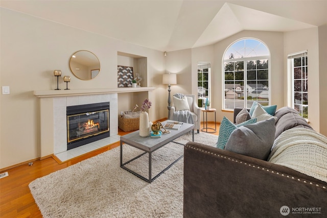 living room with visible vents, a tiled fireplace, baseboards, wood finished floors, and vaulted ceiling