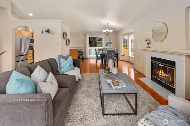 living area with arched walkways, a fireplace, vaulted ceiling, light wood-type flooring, and a chandelier
