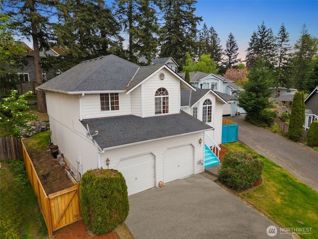 traditional-style house with roof with shingles, fence, an attached garage, and driveway