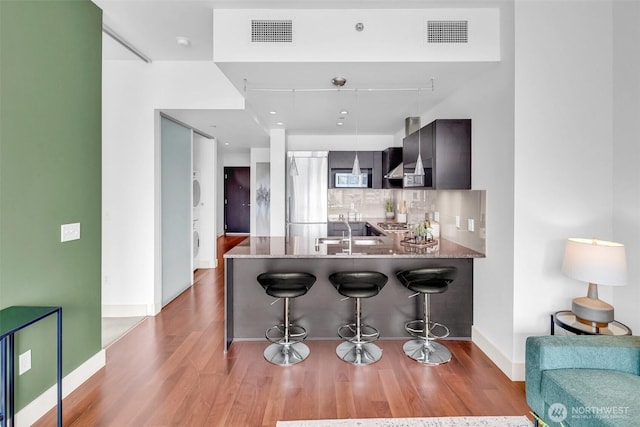 kitchen with wood finished floors, stainless steel appliances, a kitchen bar, a peninsula, and decorative backsplash