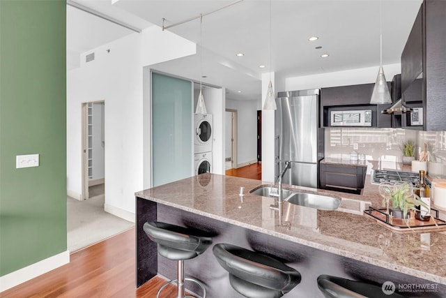kitchen featuring estacked washer and dryer, stainless steel refrigerator, a sink, light wood finished floors, and modern cabinets