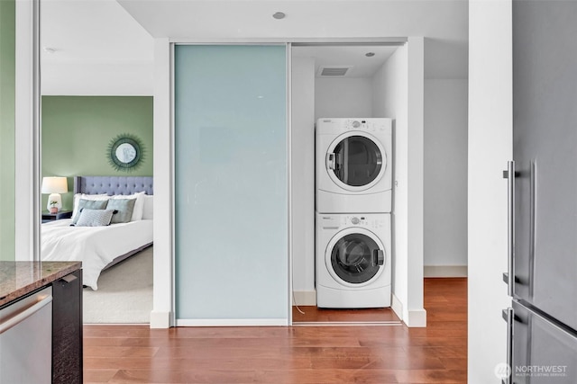clothes washing area with stacked washer and clothes dryer, wood finished floors, and baseboards