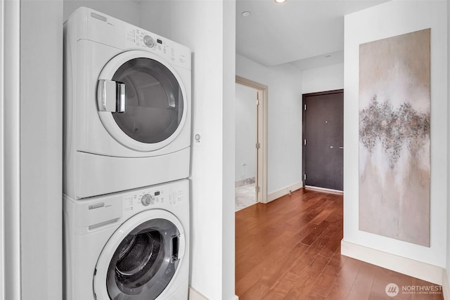 washroom featuring estacked washer and dryer, wood finished floors, and baseboards