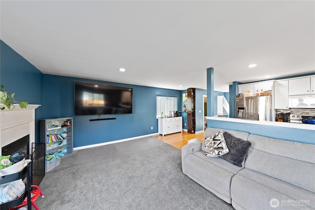 living area featuring baseboards, a glass covered fireplace, recessed lighting, and light colored carpet