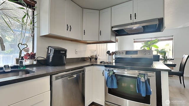 kitchen featuring white cabinets, a sink, dark countertops, under cabinet range hood, and appliances with stainless steel finishes