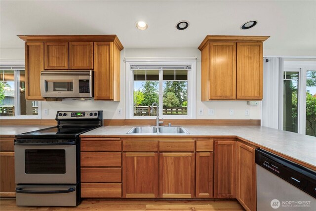 kitchen with brown cabinetry, recessed lighting, light countertops, a sink, and stainless steel appliances
