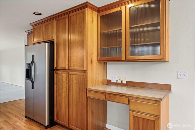 kitchen featuring glass insert cabinets, brown cabinets, built in desk, stainless steel fridge with ice dispenser, and light wood-style floors