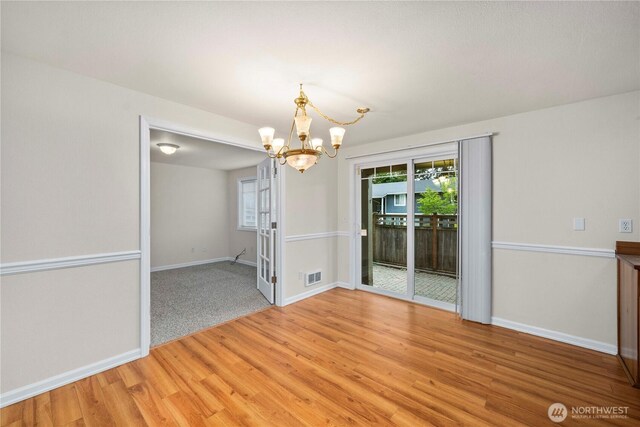 unfurnished dining area featuring baseboards, a notable chandelier, visible vents, and light wood-style flooring