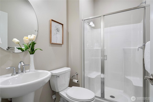 bathroom featuring a sink, a stall shower, and toilet