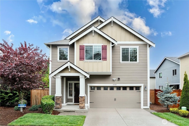 craftsman inspired home featuring board and batten siding, driveway, a garage, fence, and stone siding