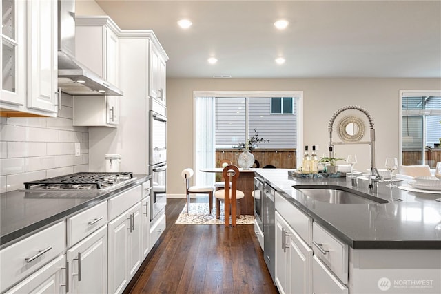 kitchen featuring dark wood-type flooring, wall chimney exhaust hood, white cabinetry, a sink, and appliances with stainless steel finishes