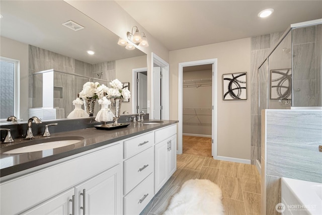 full bathroom featuring visible vents, a sink, a walk in closet, and a stall shower