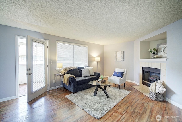 living area featuring a tiled fireplace, a textured ceiling, and wood finished floors