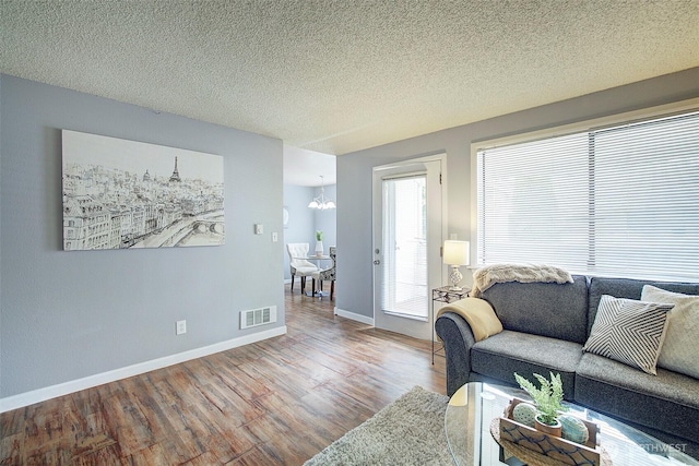 living room with baseboards, wood finished floors, visible vents, and an inviting chandelier