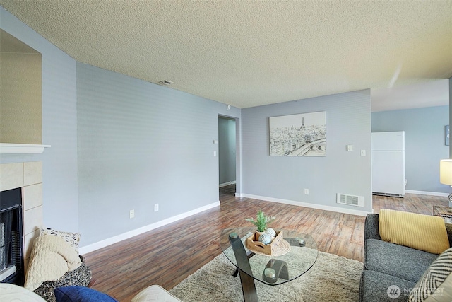 living area featuring a textured ceiling, a tile fireplace, wood finished floors, and visible vents